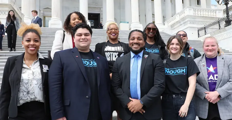 A group of people in suits and t-shirts standing in front of a staircase. Multiple t-shirts read I Am Enough.